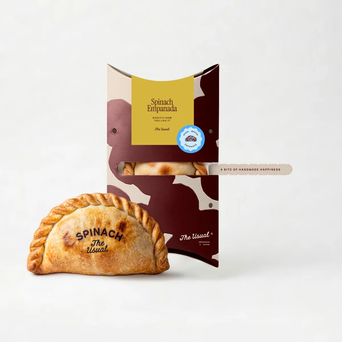 A golden empanada stamped SPINACH, The Usual, beside its burgundy pack